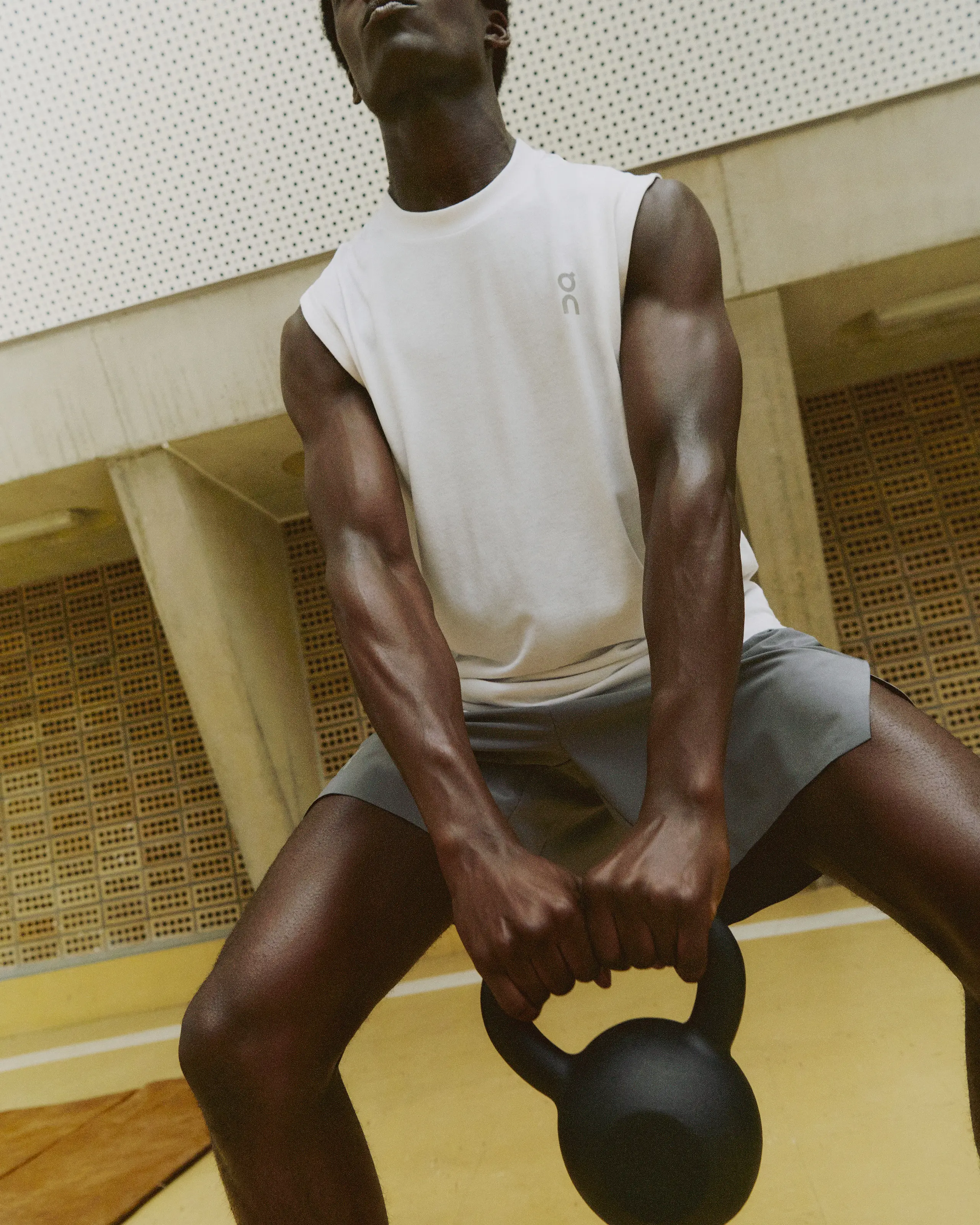 An athlete in an On tank top and shorts lifting a kettlebell indoors.