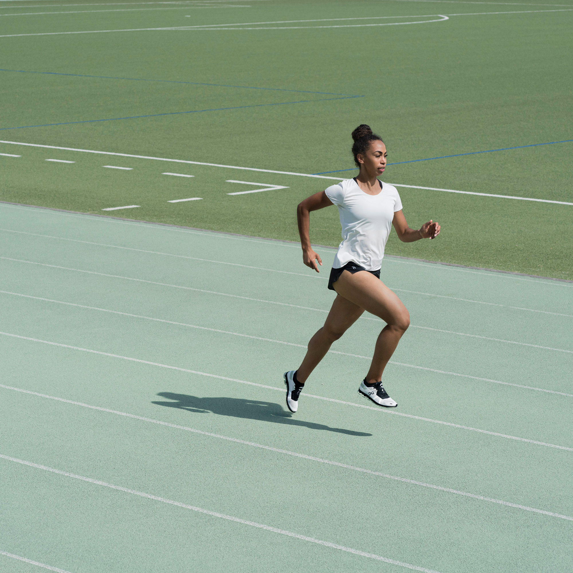 Eine Frau rennt auf einer grünen Laufbahn mit einem Fussballfeld im Hintergrund