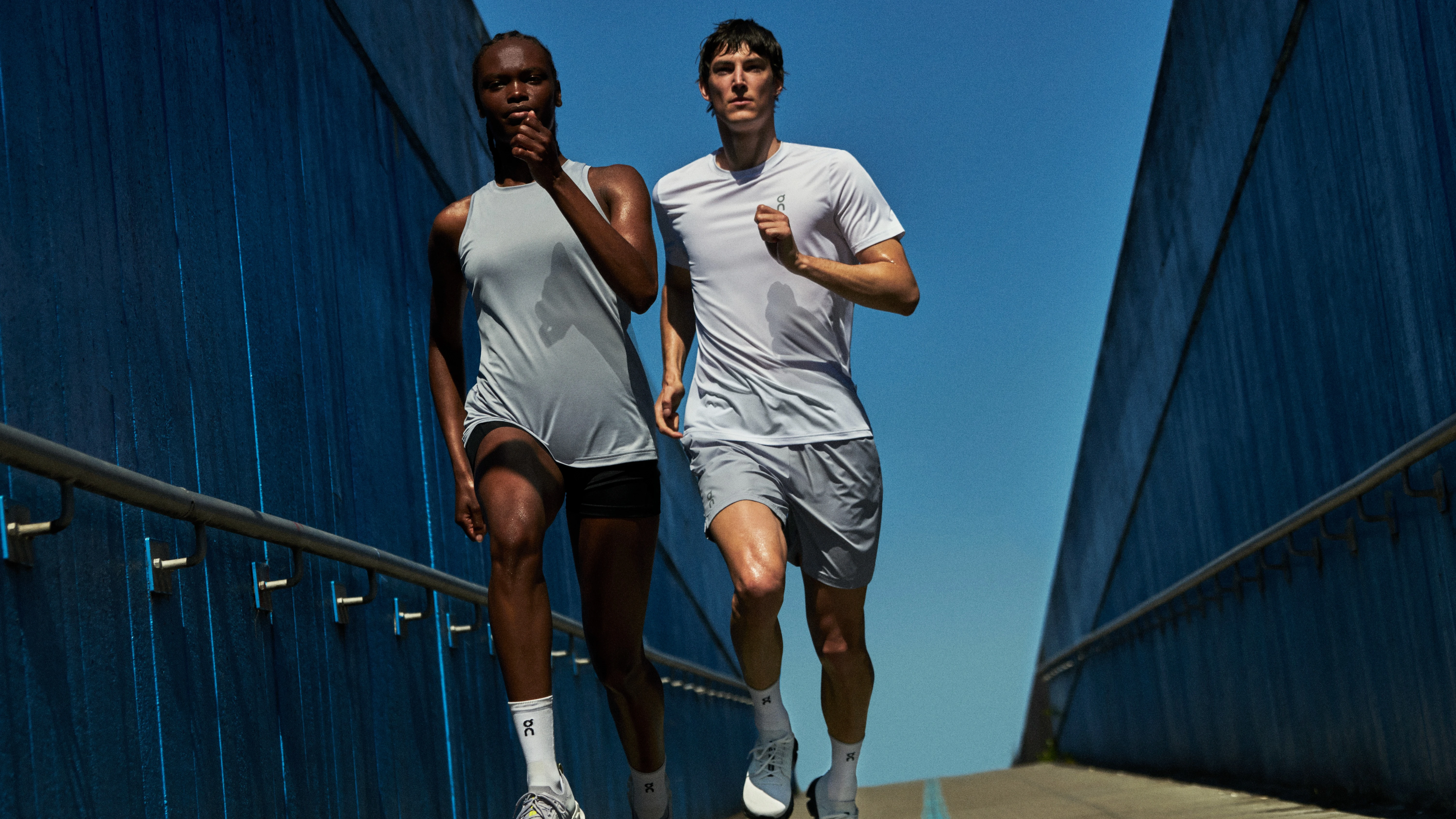 Two men in On running gear run side-by-side across a bridge.