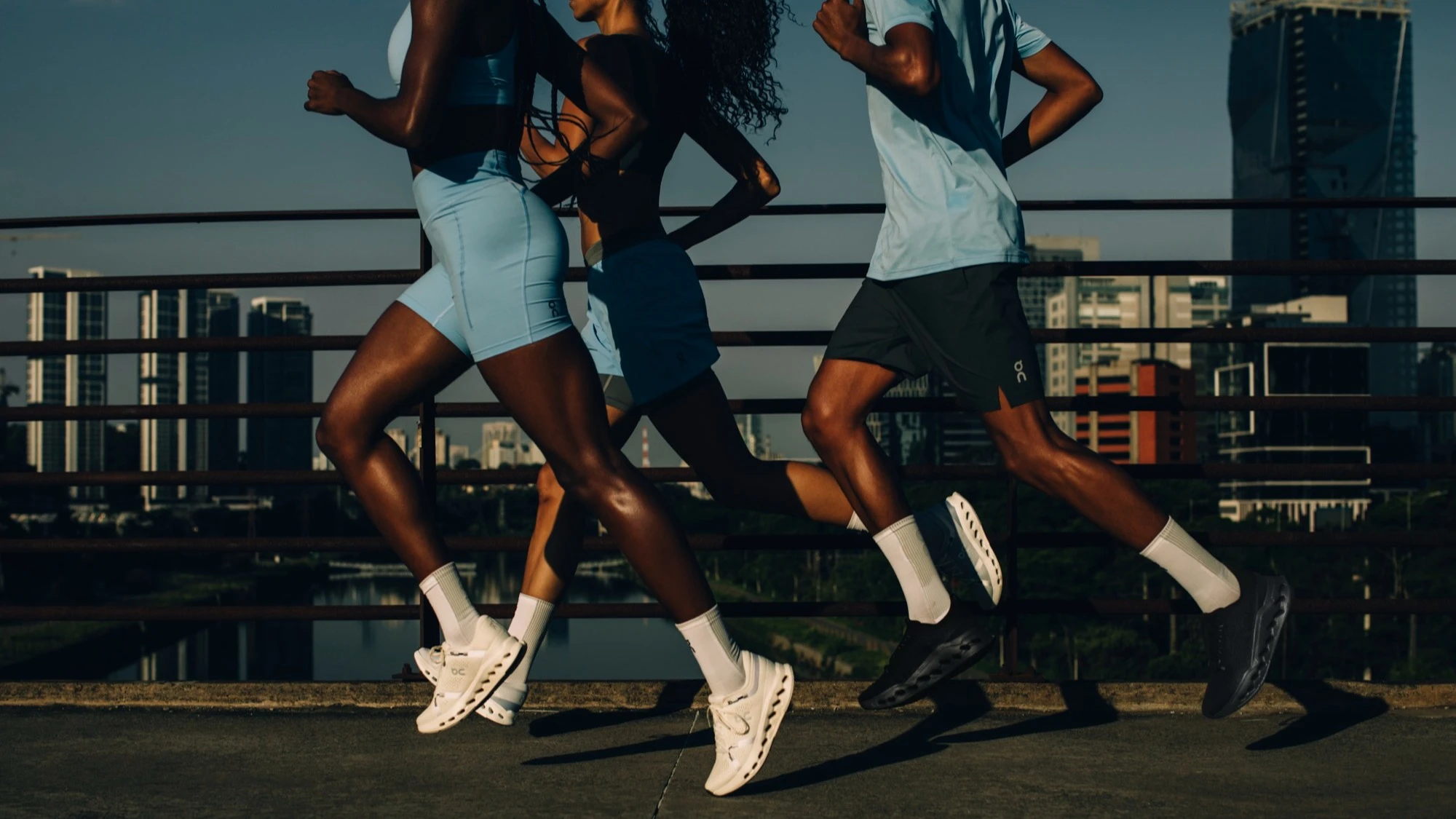 Three runners crossing a city bridge, their heads out of frame.