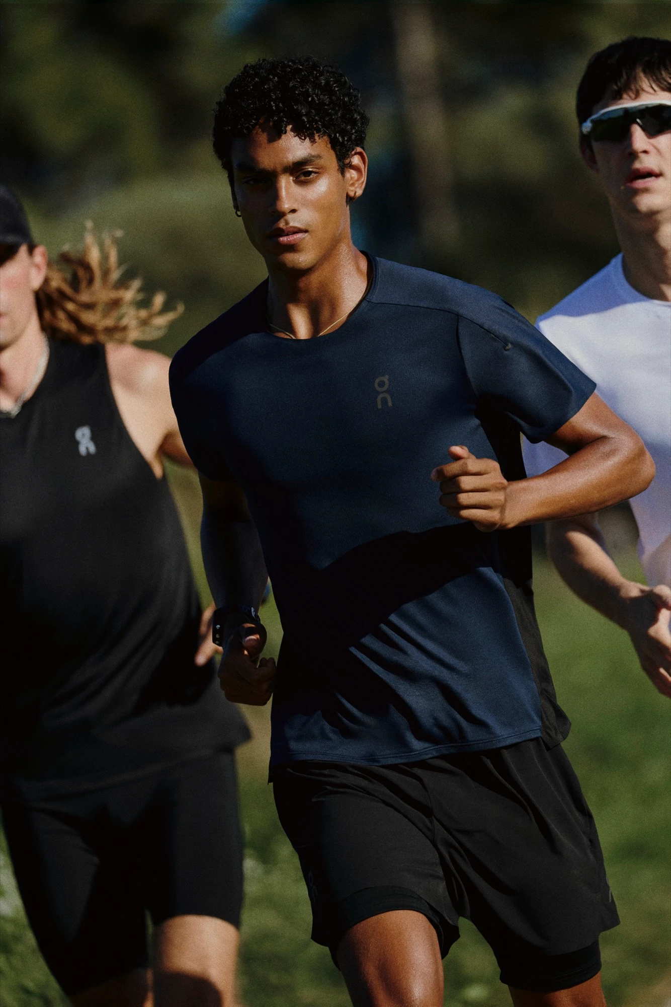 Three runners jogging towards the camera, with a green grass background.