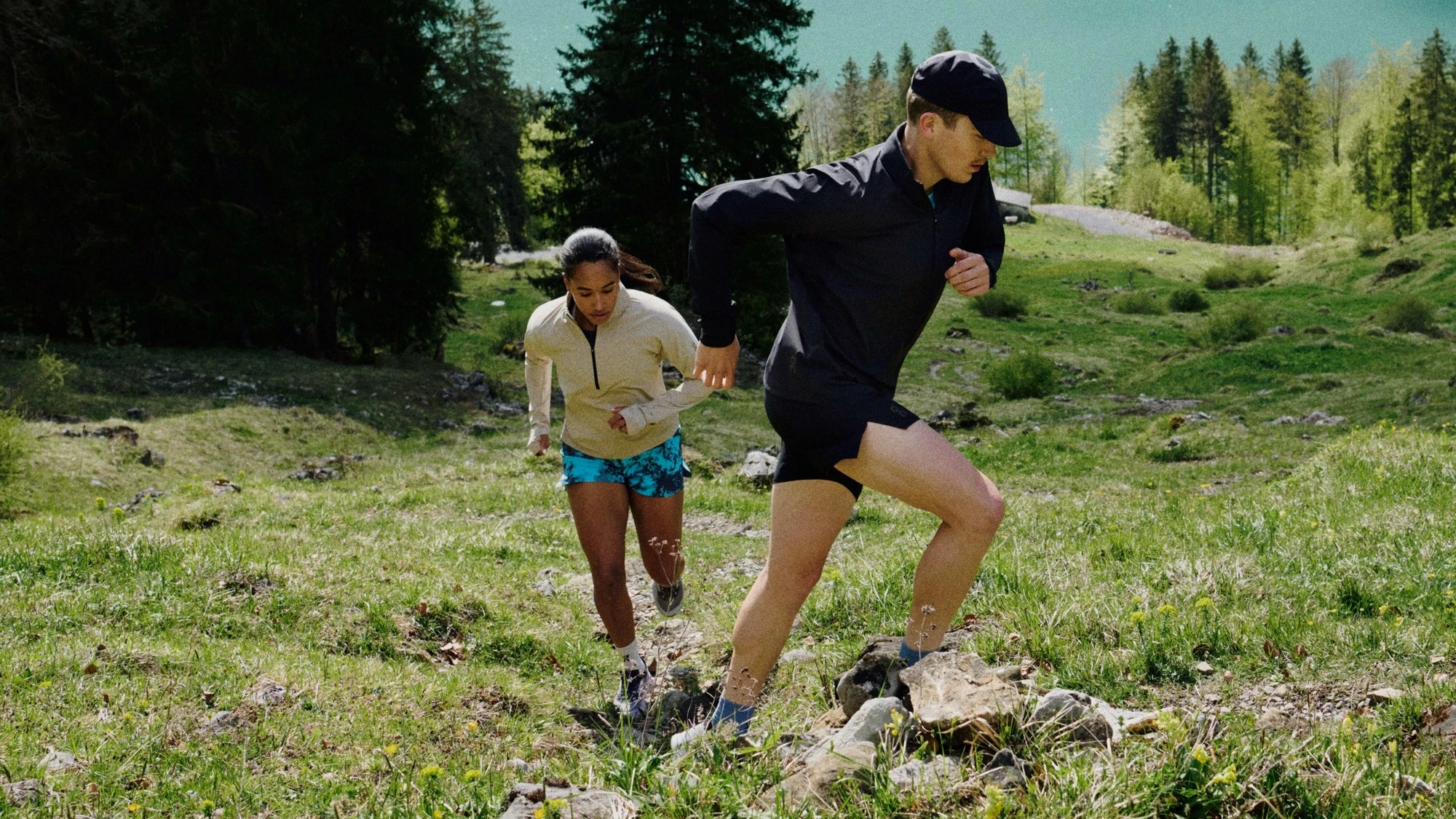 Two runners running up a mountainside with a lake in the background.