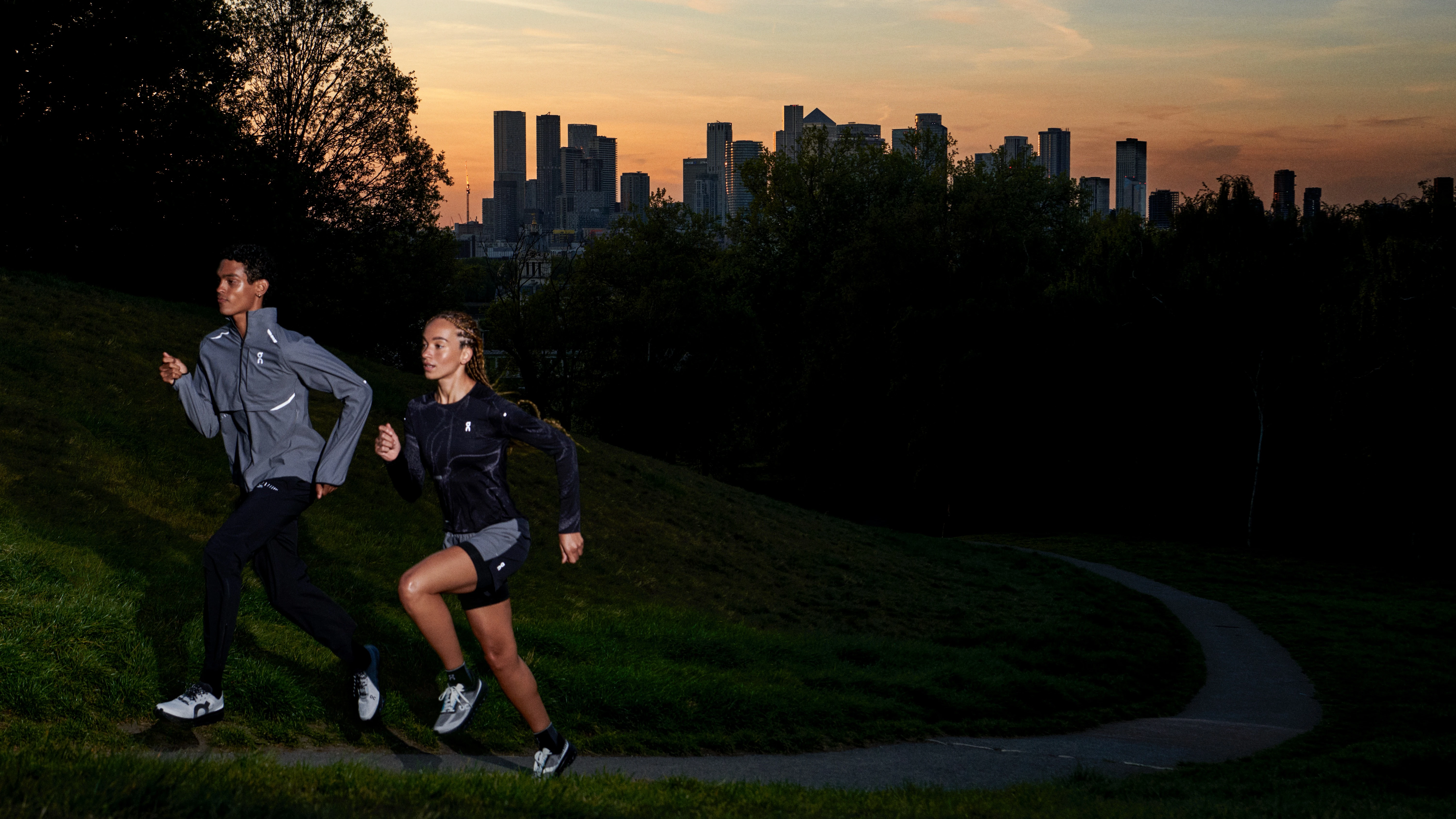 Two runners running uphill at sunrise with the city in the background.