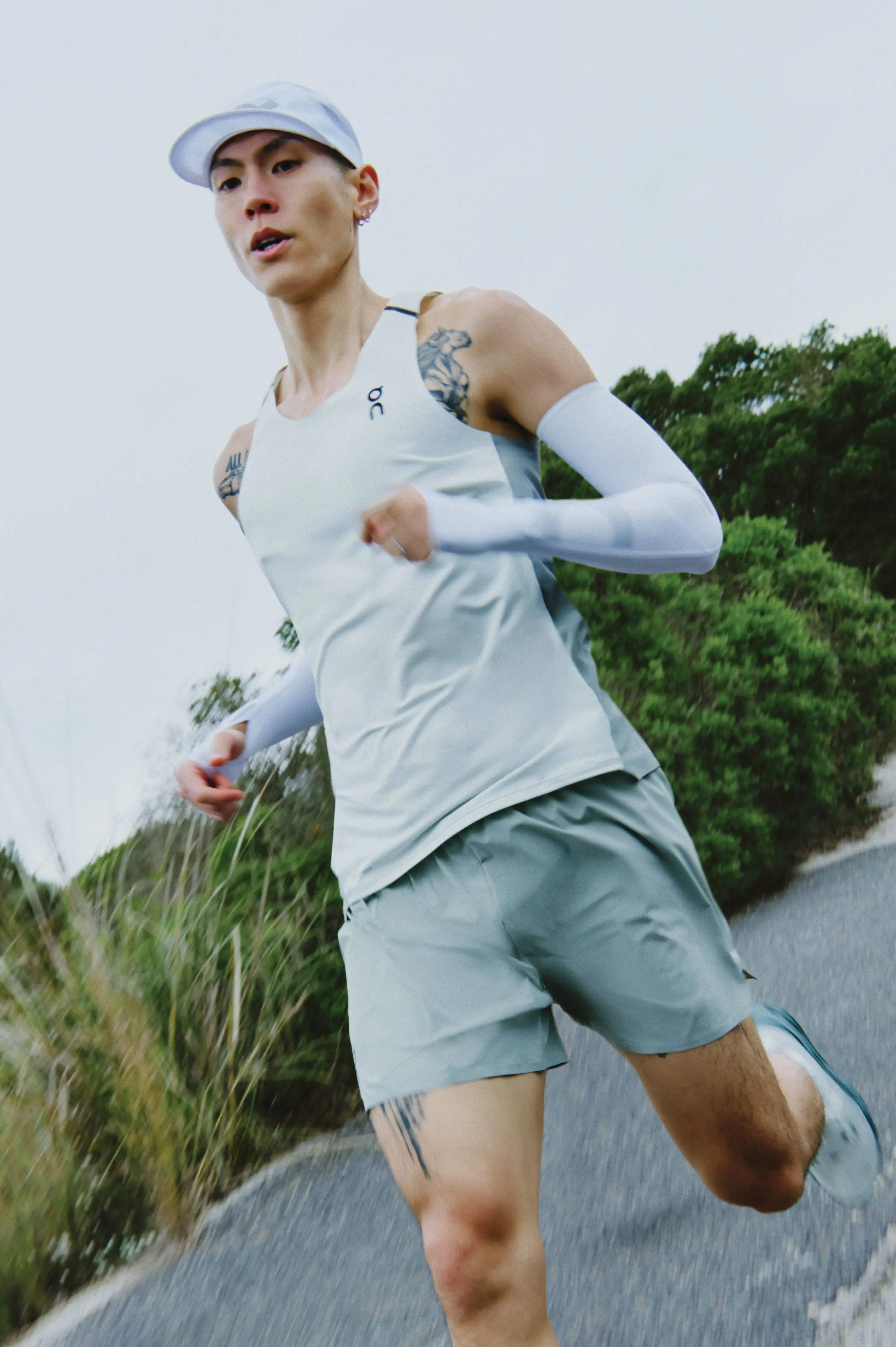 A runner in On gear mid-stride, running on a concrete path with greenery on the sides.