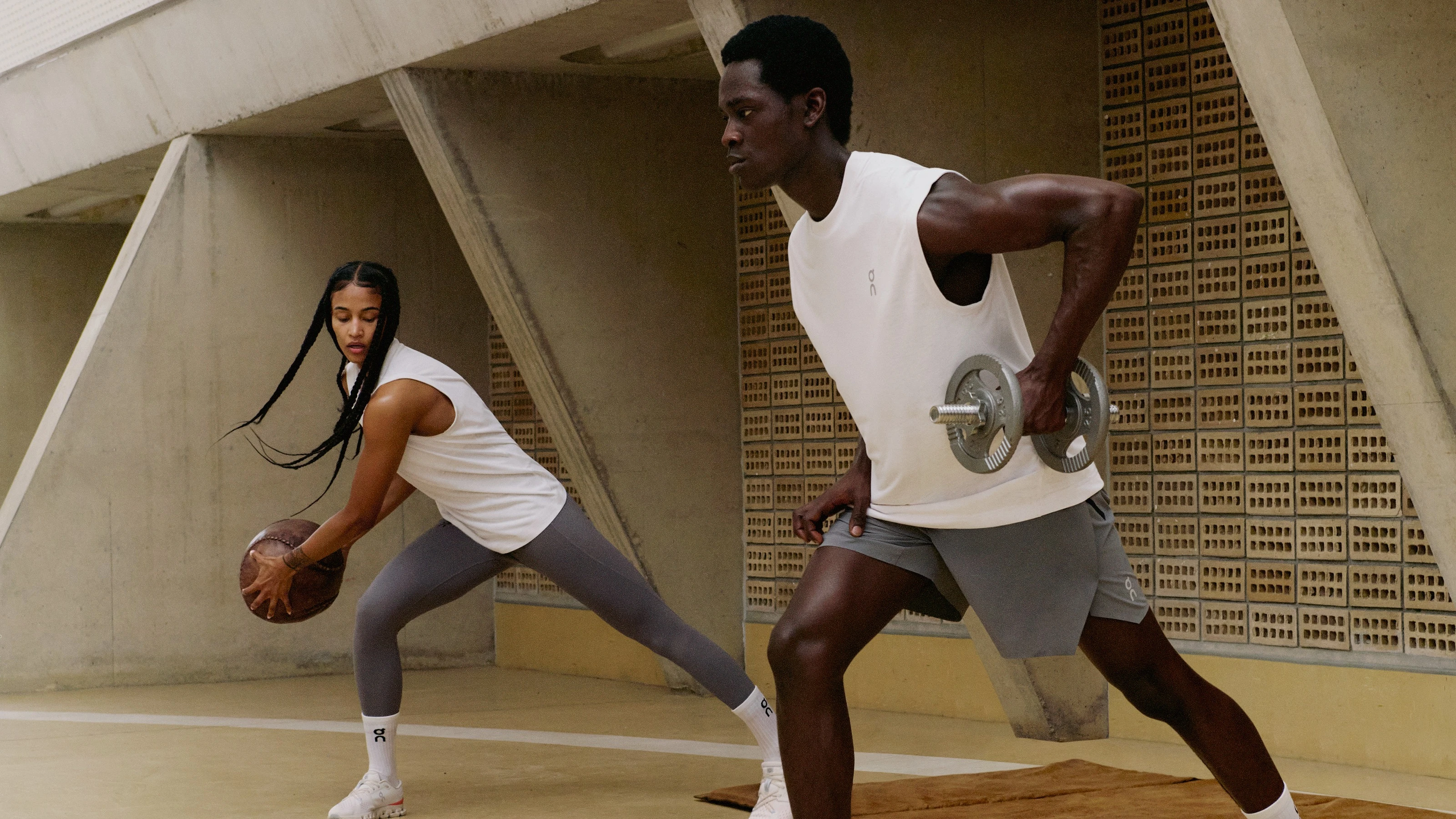 Two athletes in On workout apparel performing strength training exercises indoors.