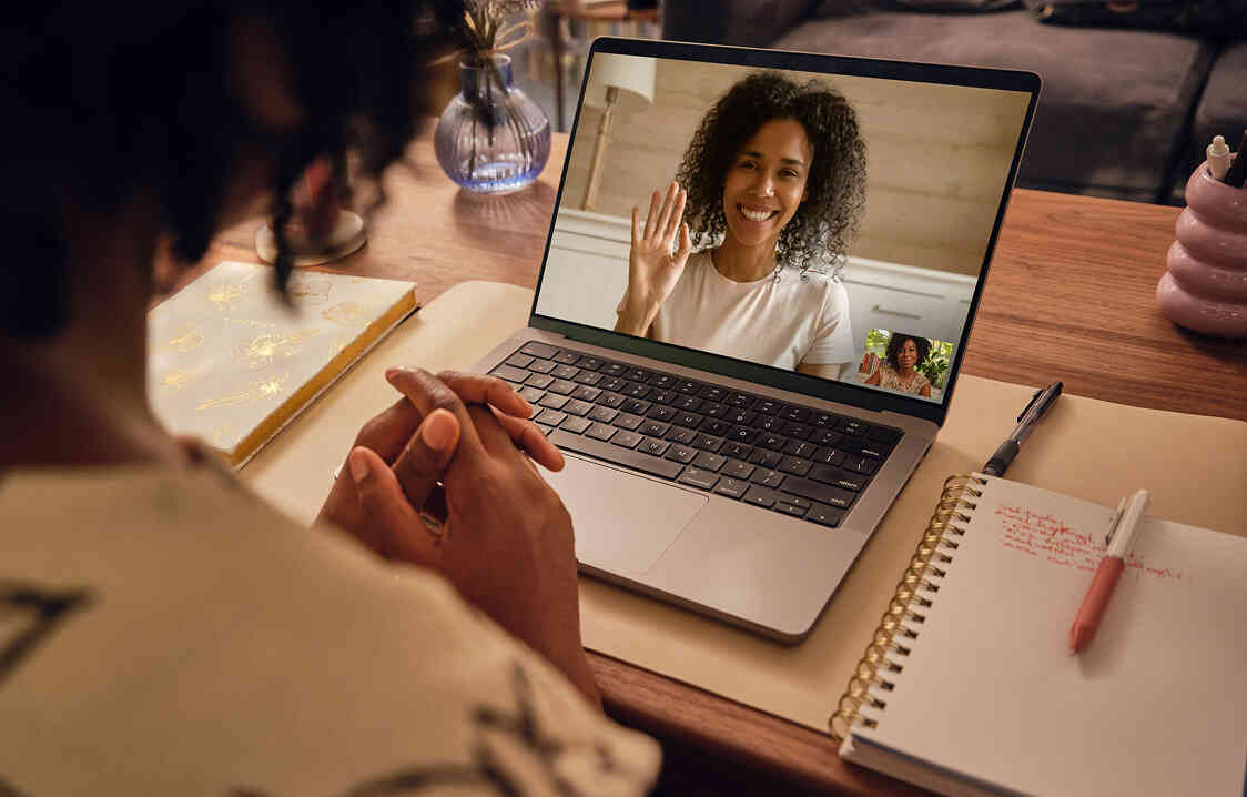 Woman waving during online therapy session on laptop.