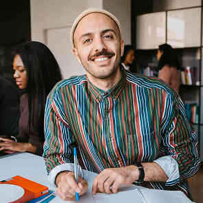 Man writing notes at desk in office and smiling.