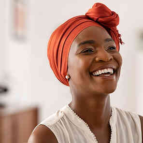 Woman smiling in orange headwrap indoors.
