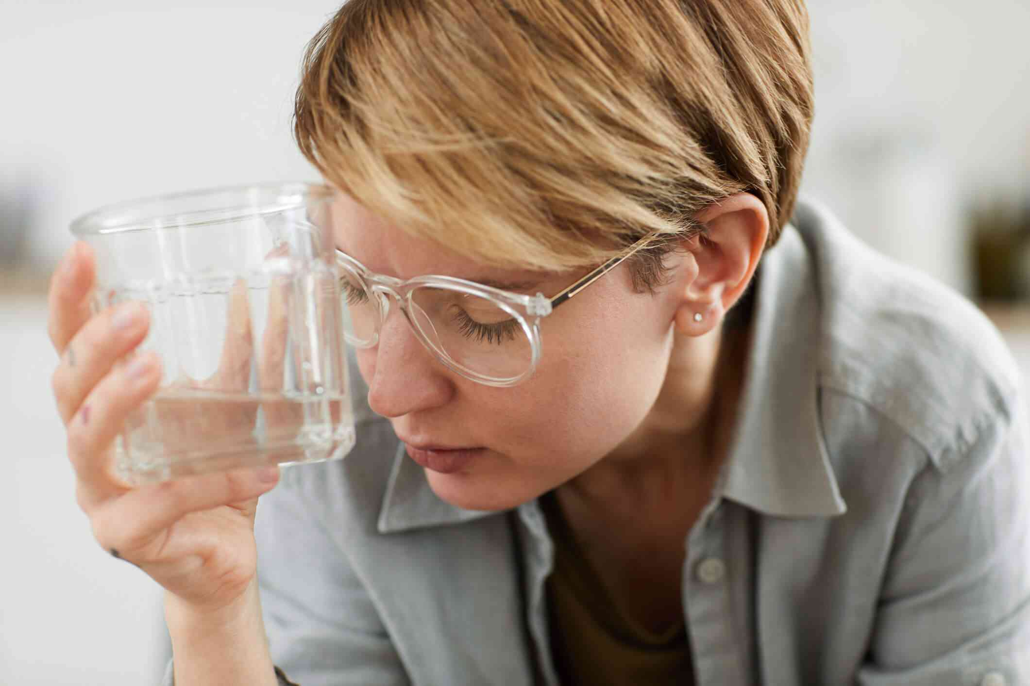 Person holding a glass of water looking stressed or fatigued.