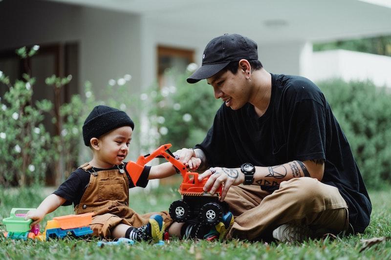 Adult and child playing with toy truck outside.
