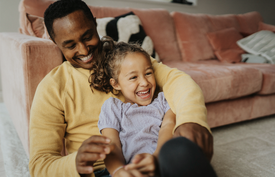 Father and daughter laughing by a couch.