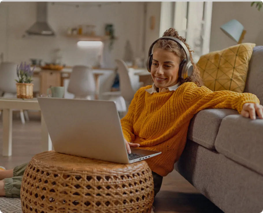 Woman using laptop with headphones by a couch at home.