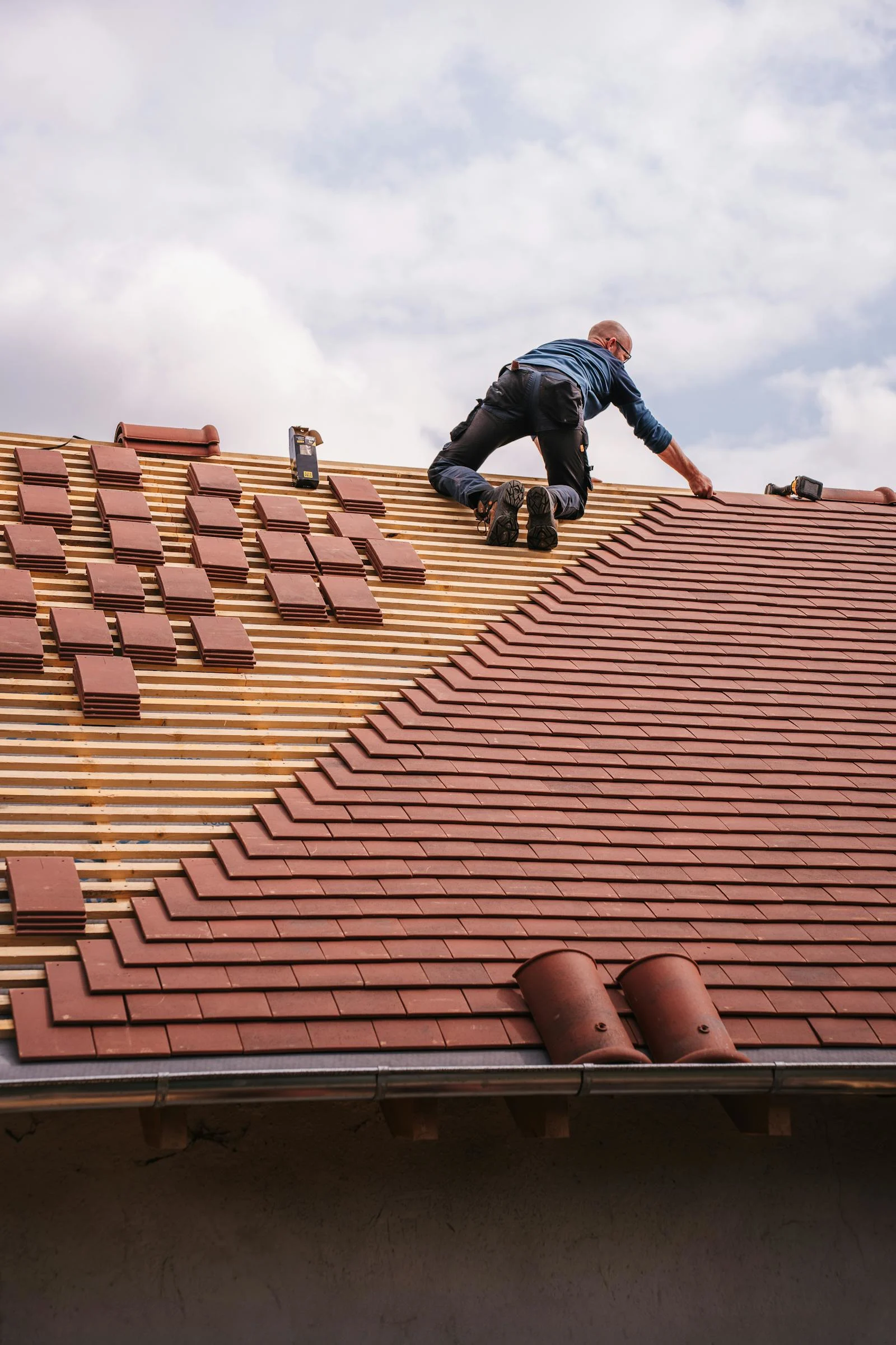 Roofer installing asphalt shingles on a steep residential roof during replacement work