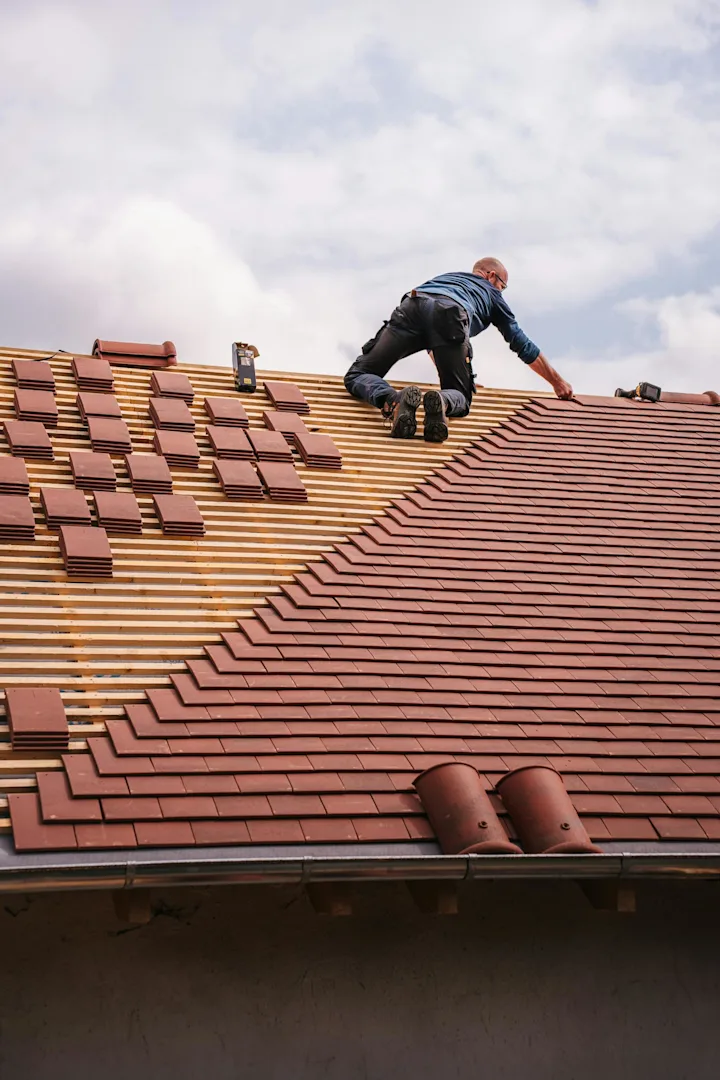 Roofer installing asphalt shingles on a steep residential roof during replacement work