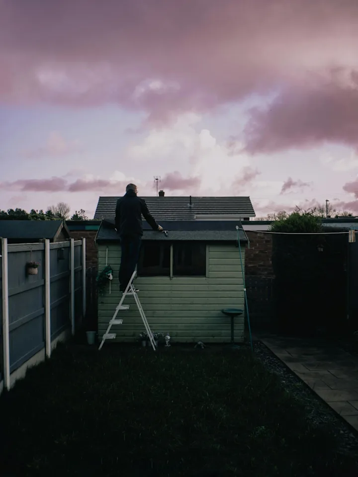 Worker standing on a ladder repairing a small residential roof after exterior damage