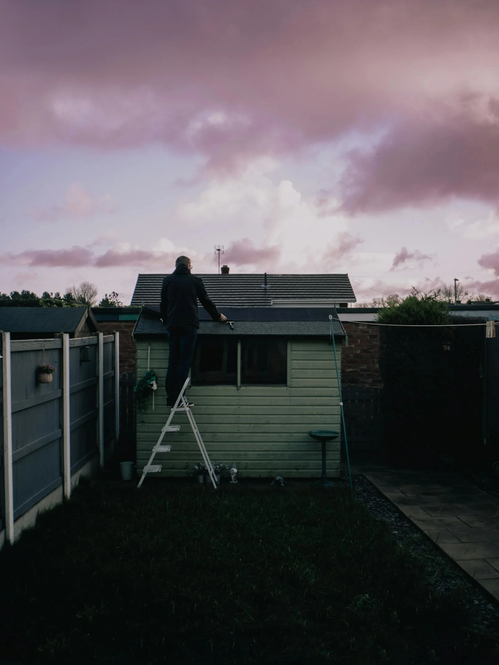 Worker standing on a ladder repairing a small residential roof after exterior damage