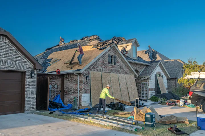 Roofing crew repairing an asphalt shingle roof while a ladder and materials are staged nearby