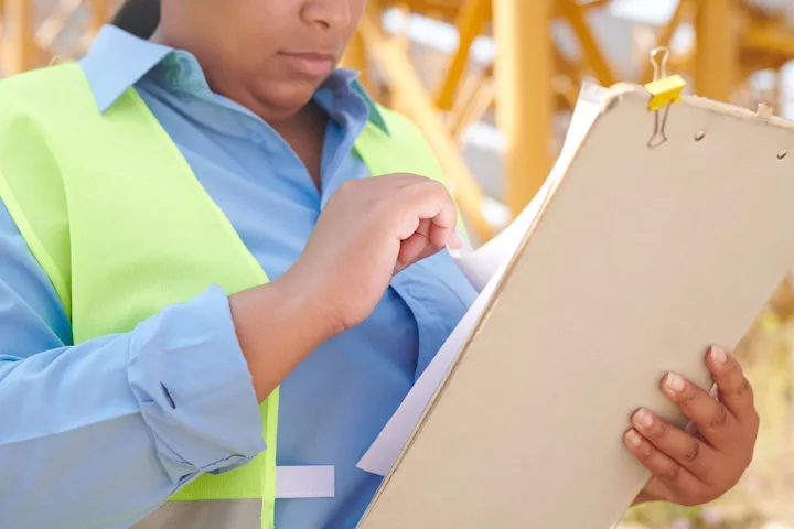 Construction professional reviewing paperwork on a clipboard at a work site