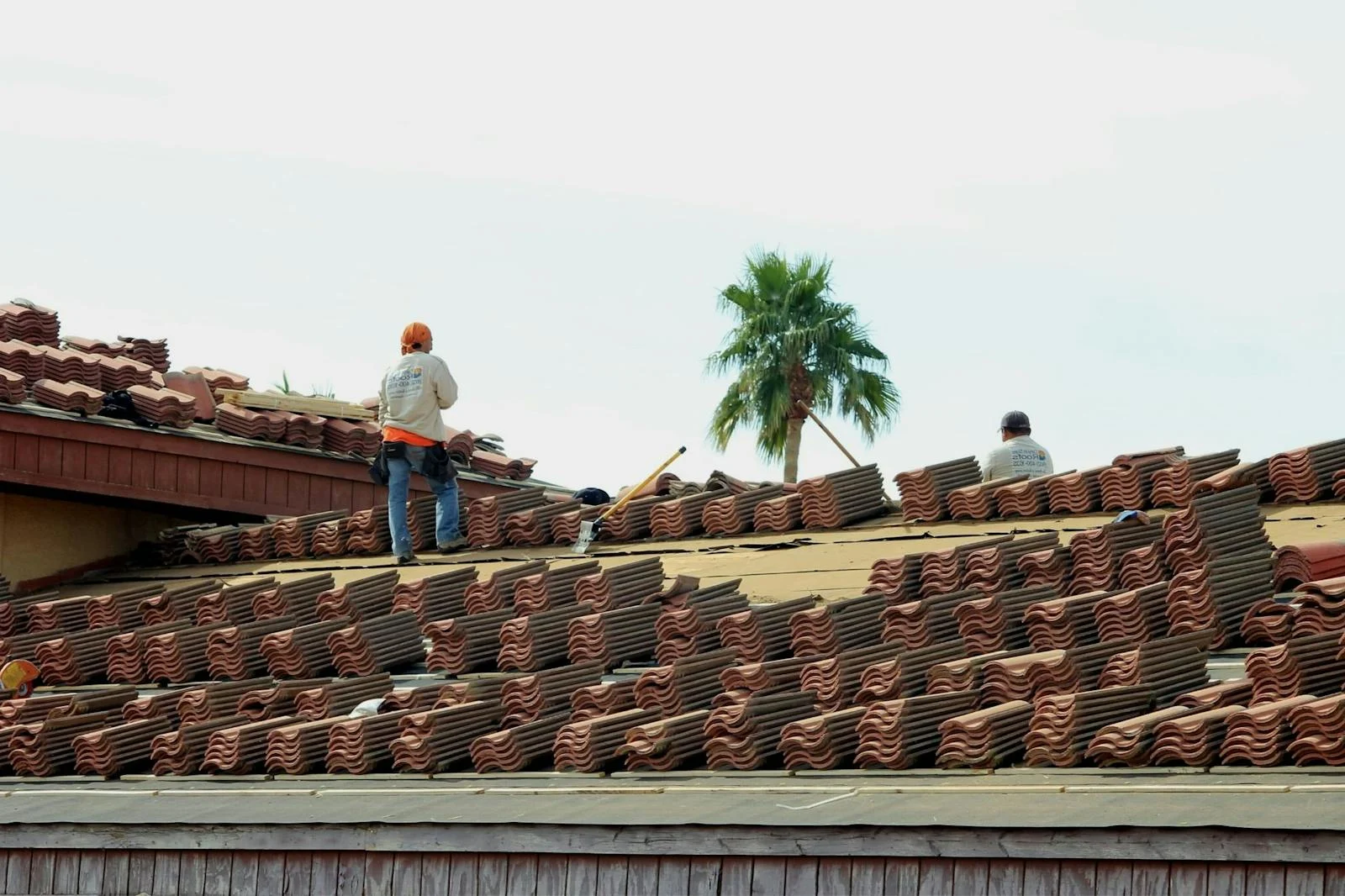 Roofing workers staging tile materials across a roof during replacement work