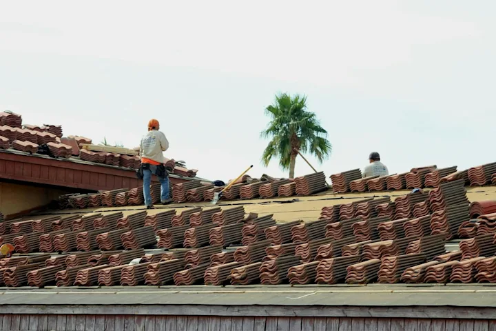 Roofing workers staging tile materials across a roof during replacement work