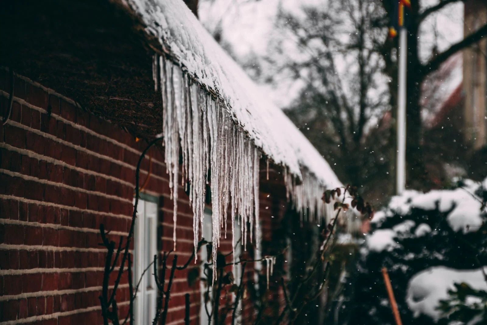 Icicles hanging from a snow-covered roof edge above a brick wall and windows