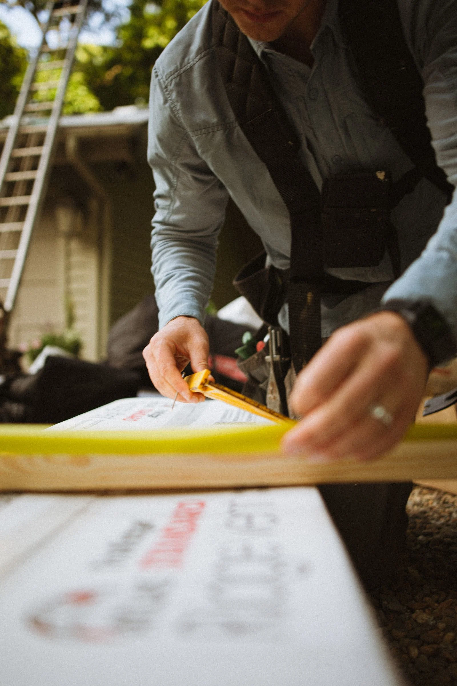 Construction worker measuring residential roofing materials with a tape measure outdoors