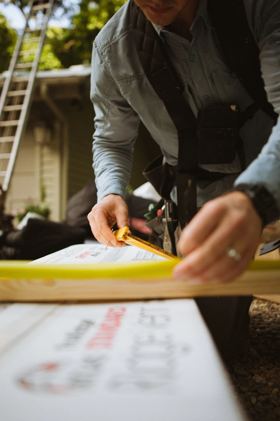Construction worker measuring residential roofing materials with a tape measure outdoors