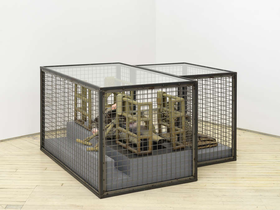 In a gallery space, a large iron sculpture resembling a cage containing another restriction device.
