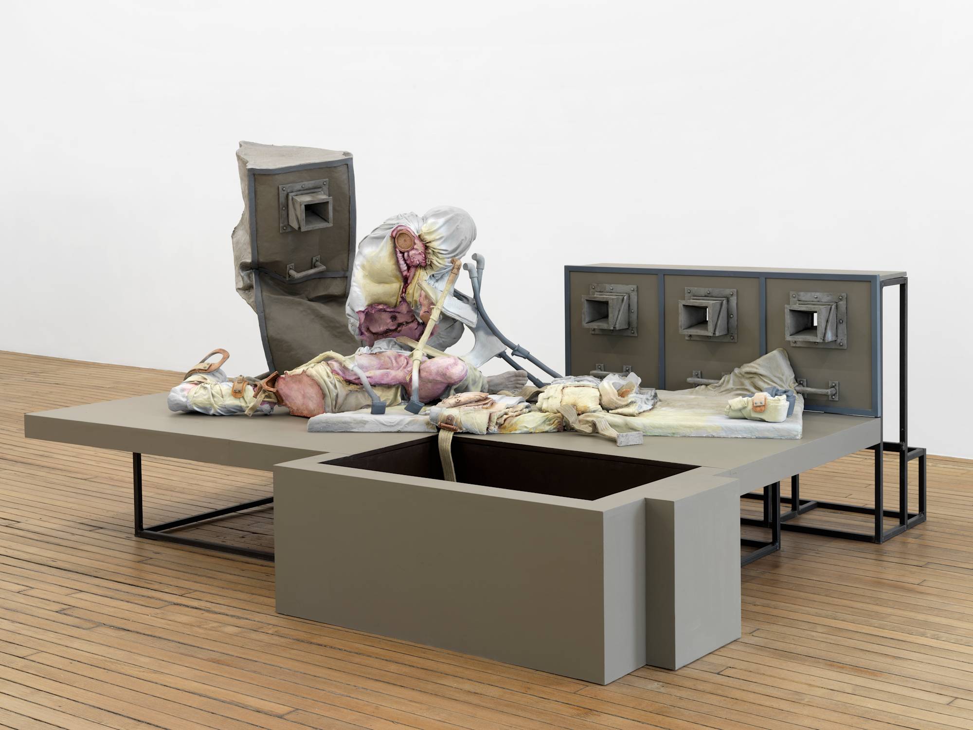 A large floor-standing sculpture depicting a combination of abstracted human forms and devices, combined with steel structures that resemble cages.