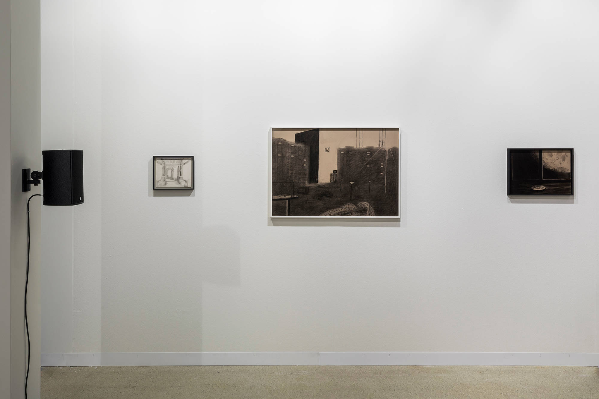 Installation view of three framed drawings hung on a wall. In the foreground there is a column on which a single speaker is hung.