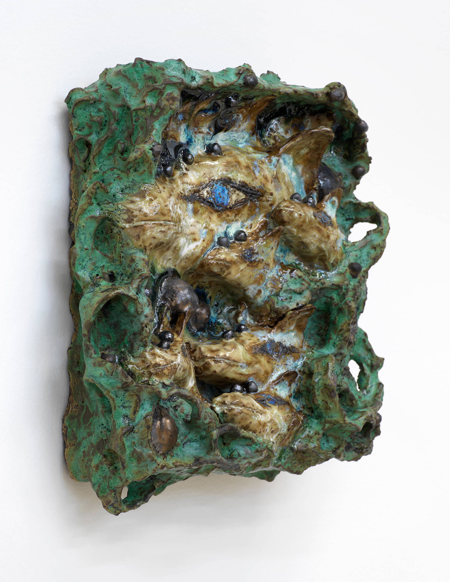 A wall mounted abstract ceramic sculpture resembling a landscape populated by different human and animal forms.