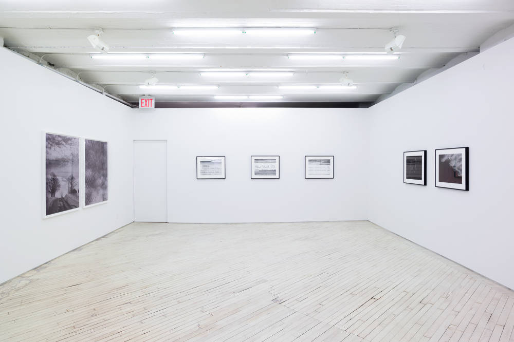 An image of the main gallery, showing 7 framed black and white photographic works. Two larger, vertical works at left, show blurred landscapes. At center, three framed horizontal photos, predominantly white with black marks and on the right wall, two framed horizontal photos predominantly black with white marks.
