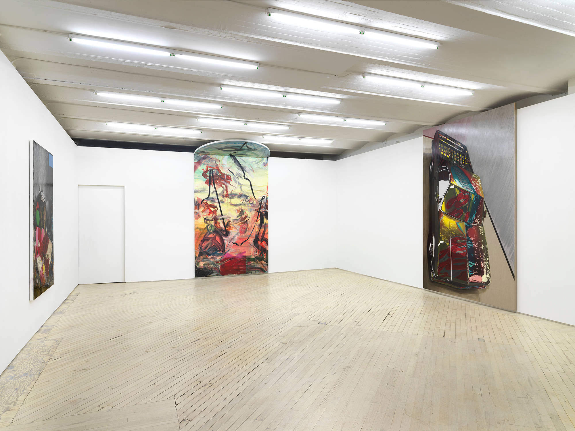 In a gallery hangs three paintings by Tom Holmes, one large columned painting that touches the ceiling with mostly abstract painterly marks, a smaller painting of a roadside memorial, and a large painting of an El Camino car standing upwards.