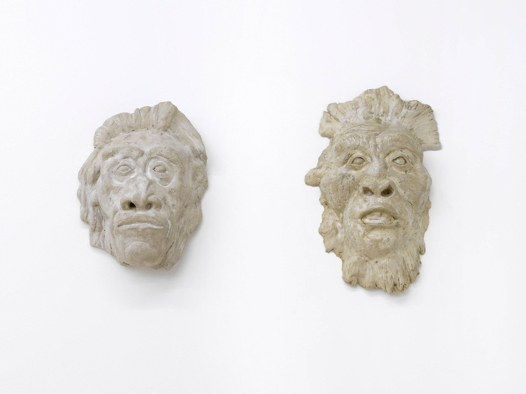 Image of two masks made from clay with expressive faces, gazing at the viewer.