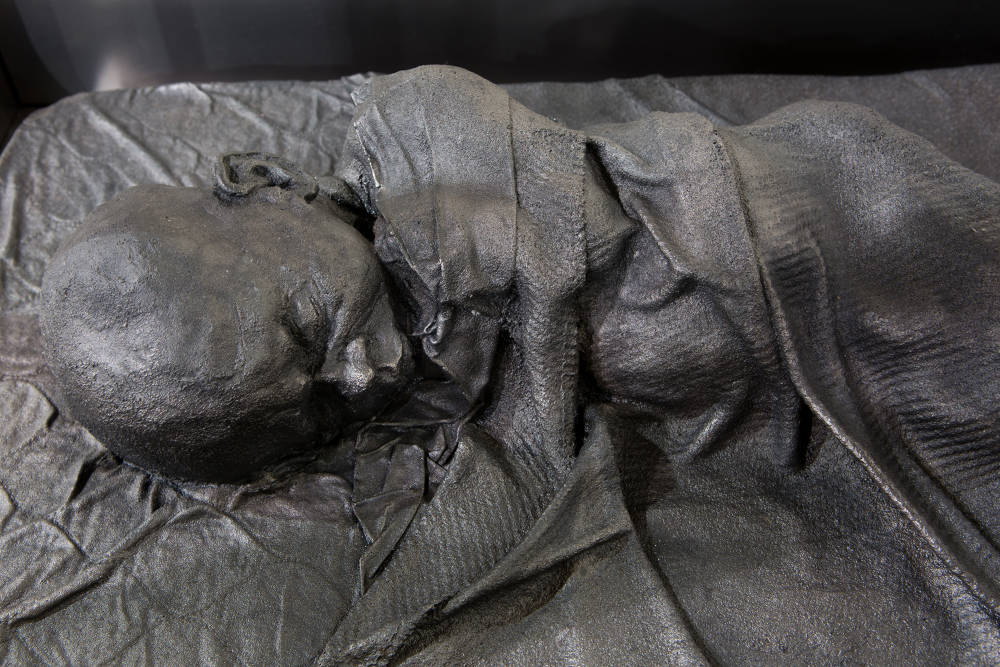 Cast iron sculpture of a child sleeping in bed wrapped in a blanket.