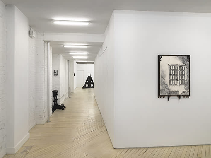 Installation view of front room of the gallery, looking down the hallway, at right, the front wall has a black and white drawing framed in an ornate black frame and the down the hallway is a black sculpture and a small wall work on the brick wall at left and a large black pyramid shape sculpture at the end of the hall in the main space.