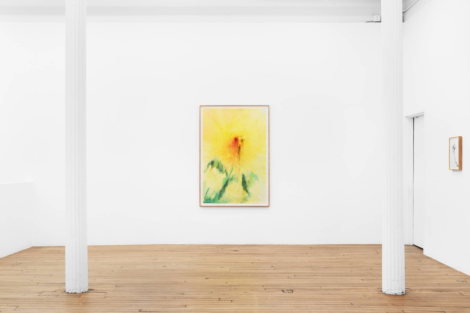 A large ink painting of a sunflower with pale yellow petals, orange-brown center, and cool green and leaves, rendered in diffuse marks, hangs framed by two white columns in a white-walled gallery with a wooden floor.