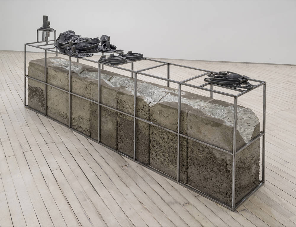 Installation view of metal and concrete sculpture, depicting metal framework atop a concrete trough, with small cast iron sculptures on top of the metal frame.