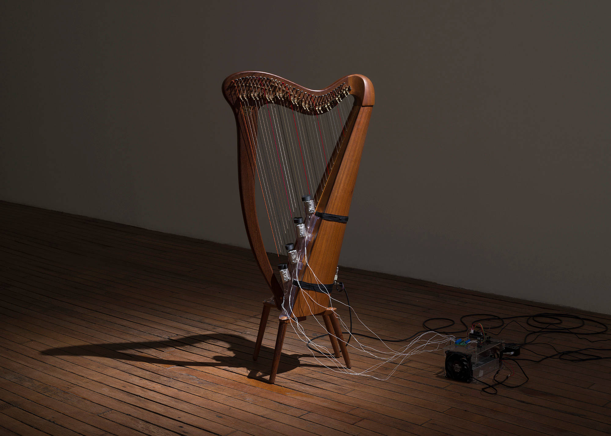 A self-playing harp sits on a wood floor under a spotlight.