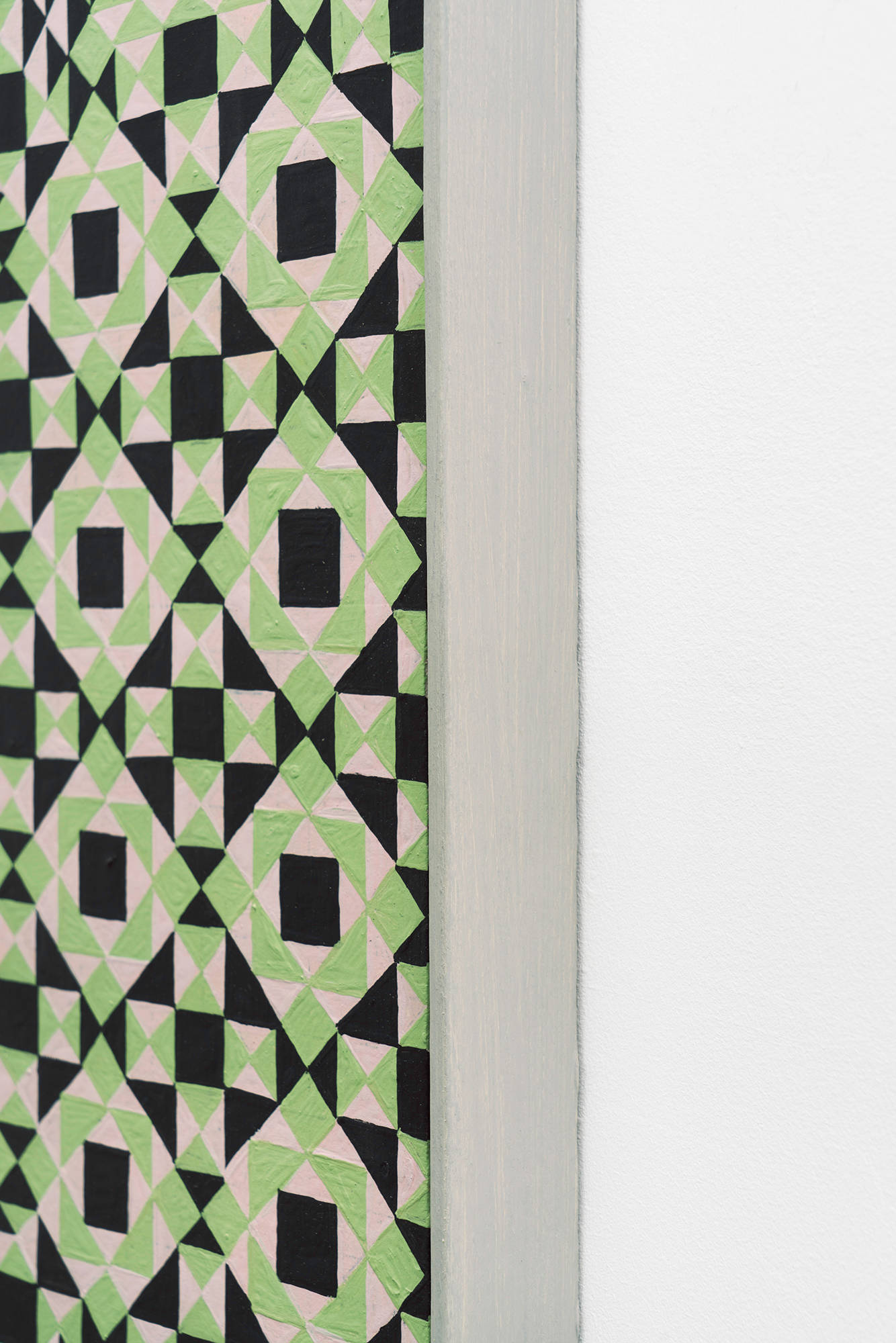 A detail shot of a colorful, symmetrical, geometric painting on board consisting of a pattern of repeating diamonds and triangles of green, light green, and dark green, in a light green artist frame.