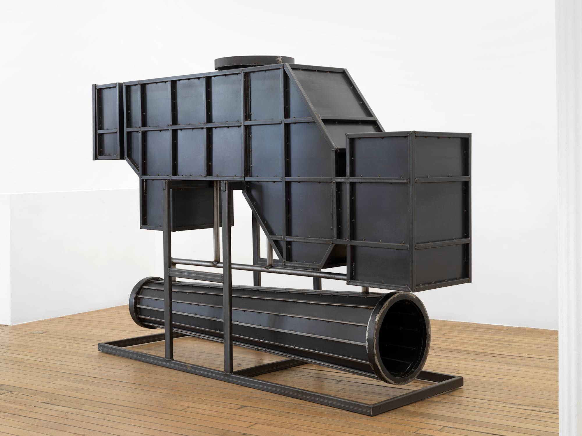 In a gallery space, a large steel sculpture resembling an abstract furnace.