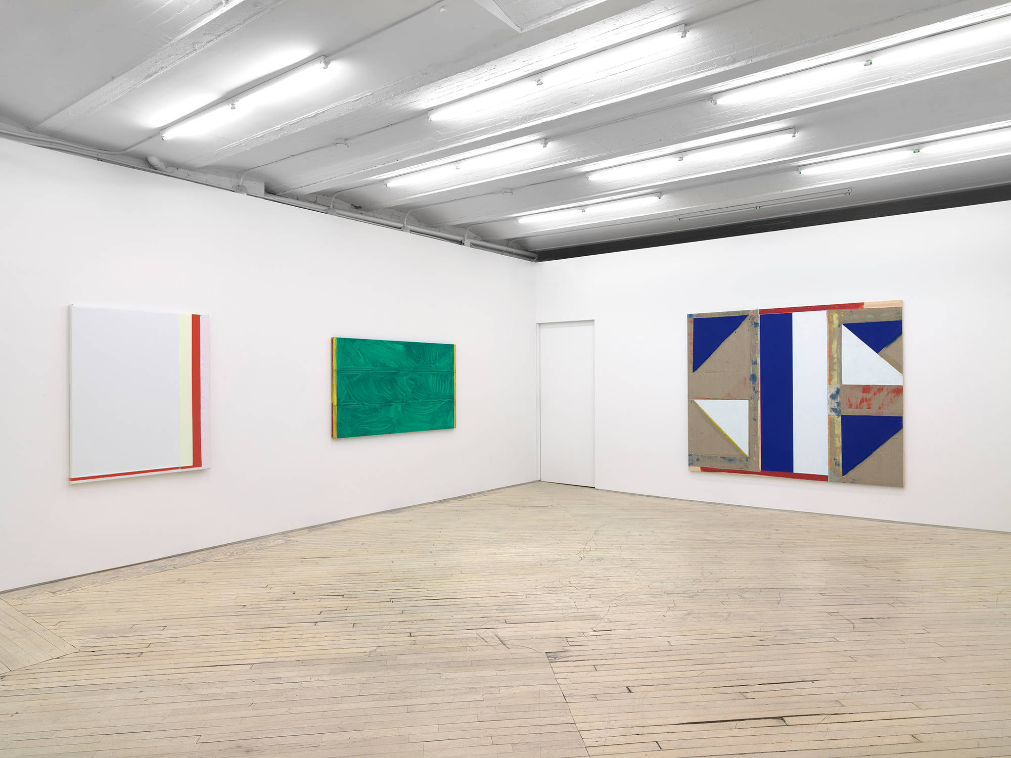 In a large gallery space, three abstract paintings in a line. On the left is a white monochrome painting with a red band of color along the right and bottom edges. In the center a horizontal green painting with a brushy surface. To the right a larger abstract painting with shapes painted in blue, white, red.