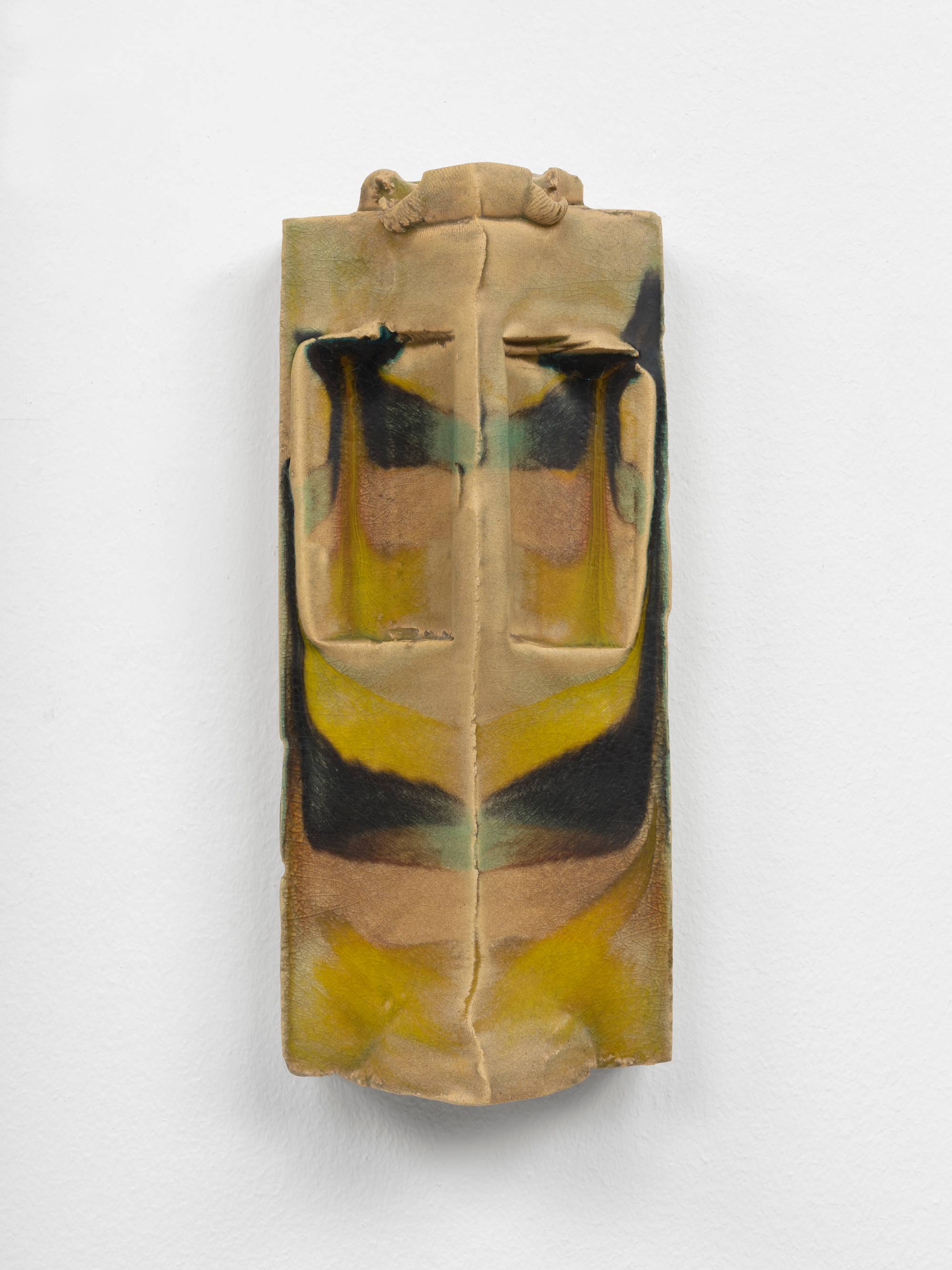 A symmetrical, wall-mounted, ceramic sculpture composed of two narrow, vertical slopes that form a peak that runs parallel to the wall. In the top half of the work a shallow pocket has been carved out of each slope and the crown has been embellished with a small, curled ornament. The sculpture is glazed in hues of brown, green, and yellow.