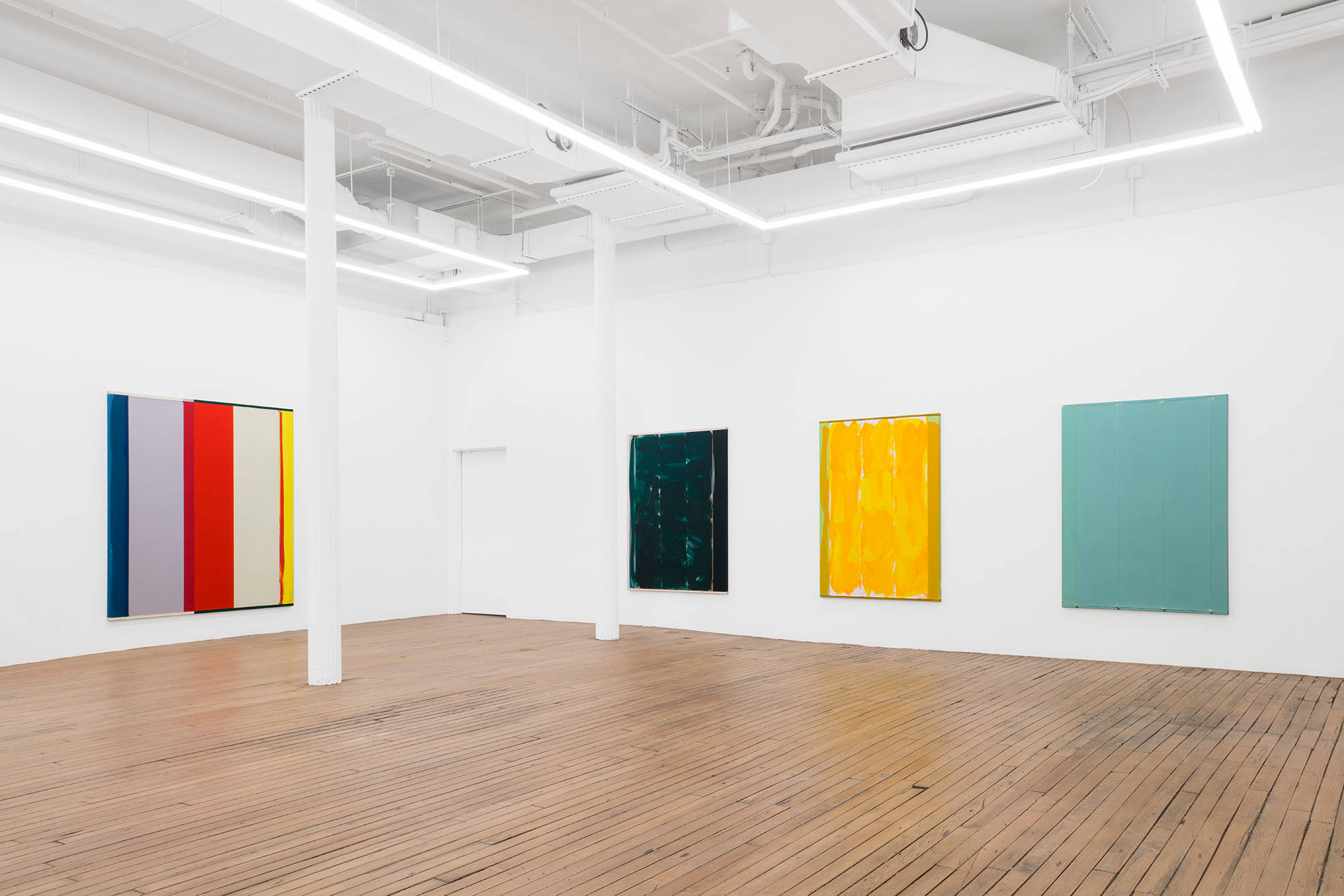 A succession of large abstract paintings depicting monochromatic fields of color in blue, yellow, and green. To the left is a larger painting depict columns of different colors.