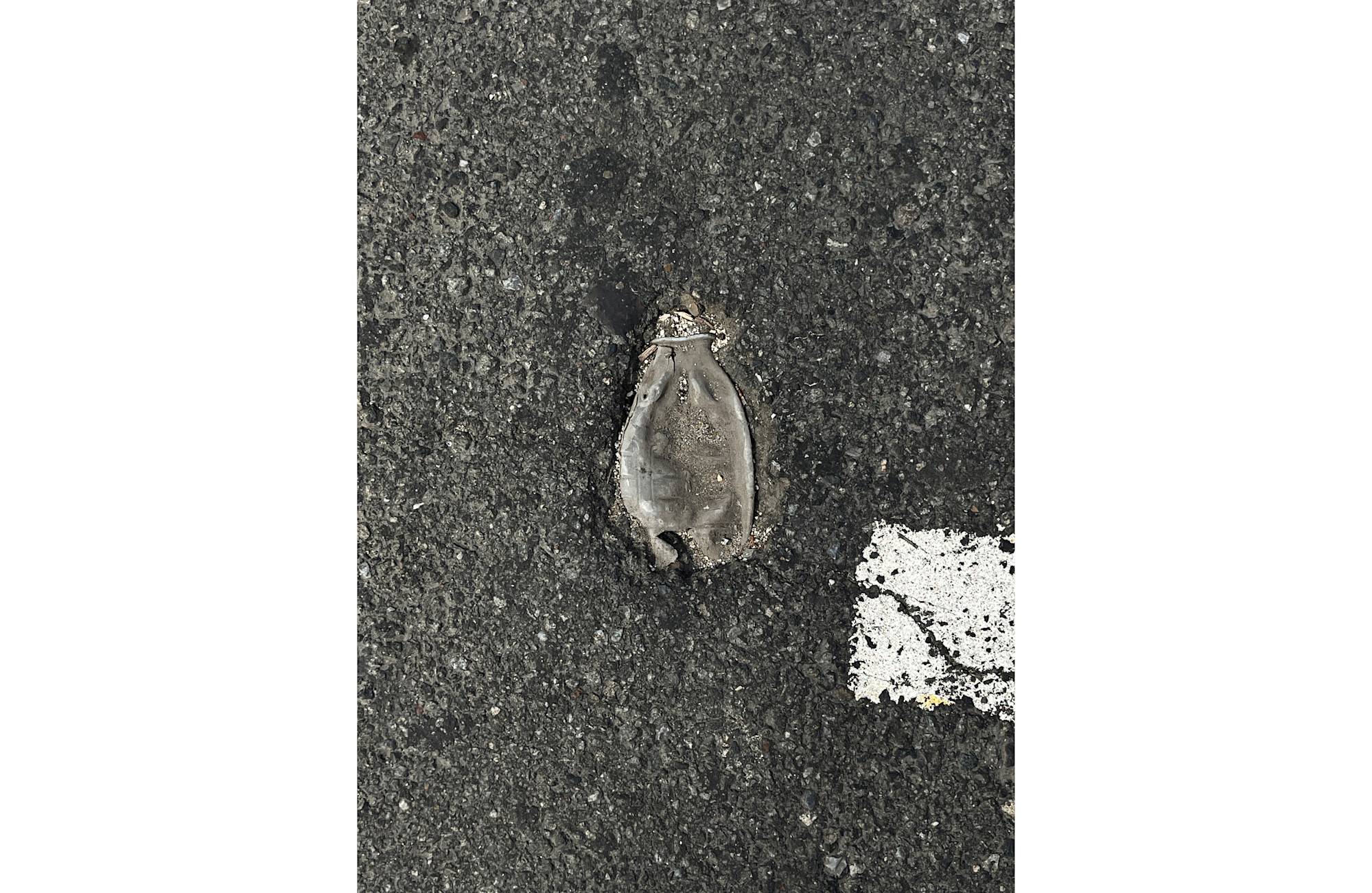 A bird's-eye view of a crushed bottle inside of a pothole on a cement road.