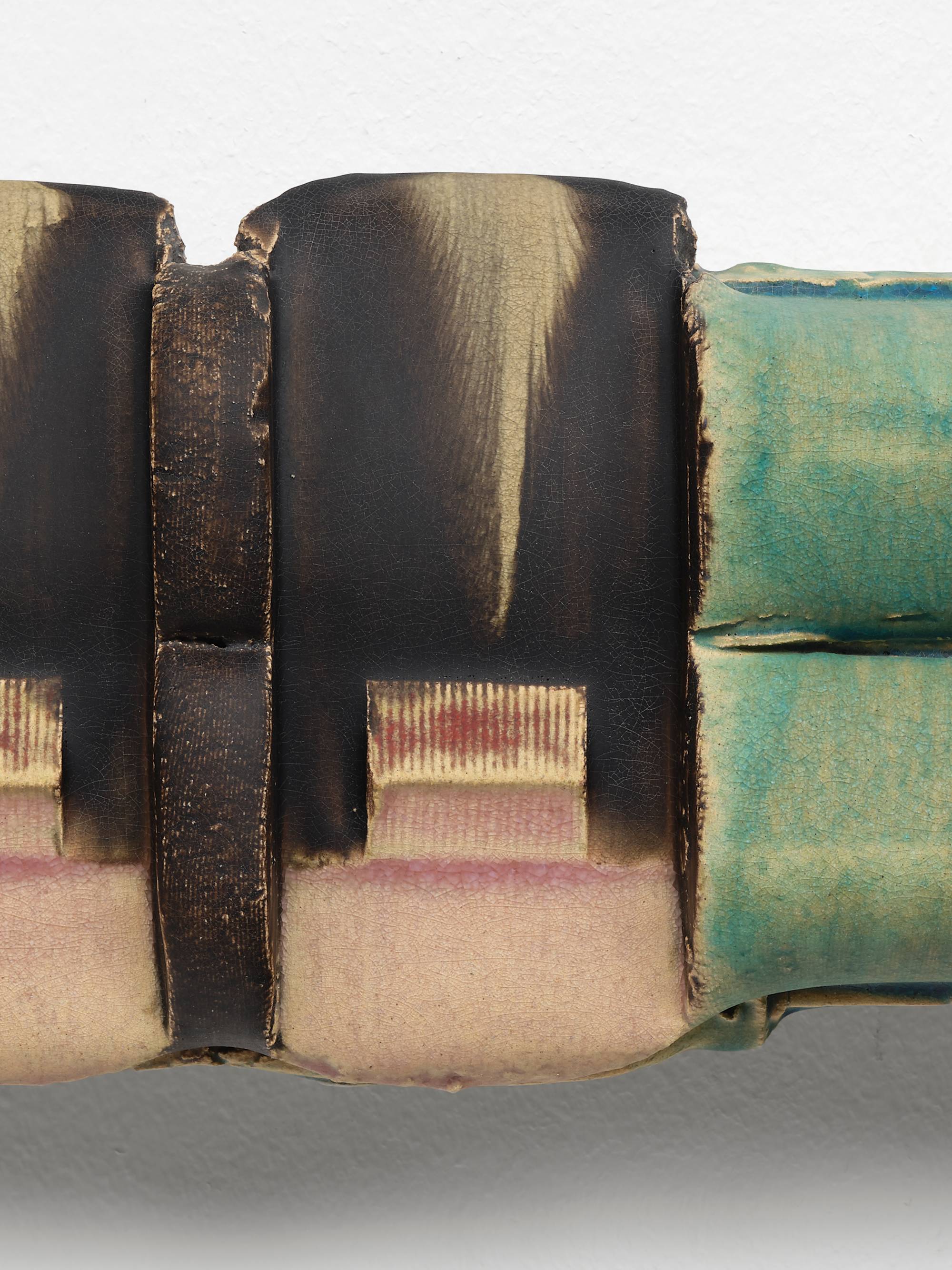 Detail of a symmetrical ceramic sculpture composed of two horizontally stacked cylinders that have been perpendicularly stamped twice towards the center and glazed in hues of aqua, pink, brown, and red.
