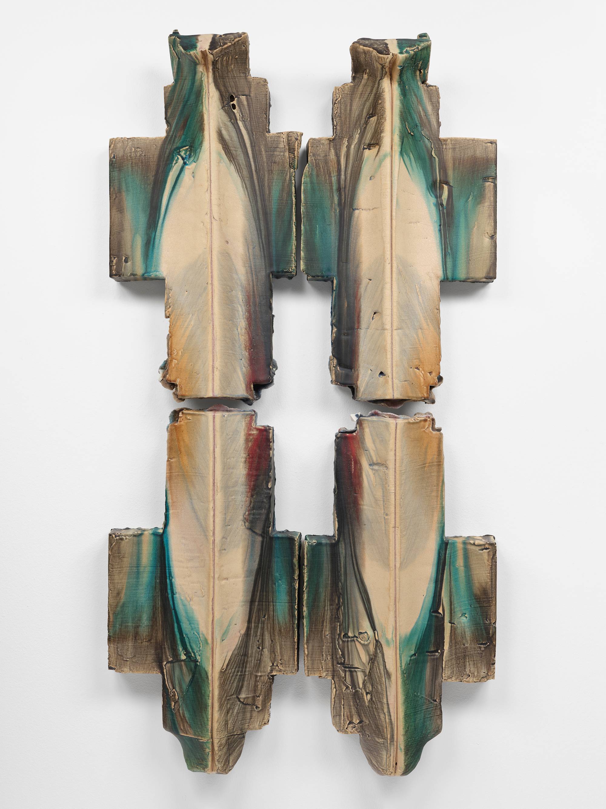 Four individual cross shaped ceramic sculptures are mounted to a white wall in a square orientation to form the shape of a pound sign (#). They are glazed in hues of aqua, red, and yellow.