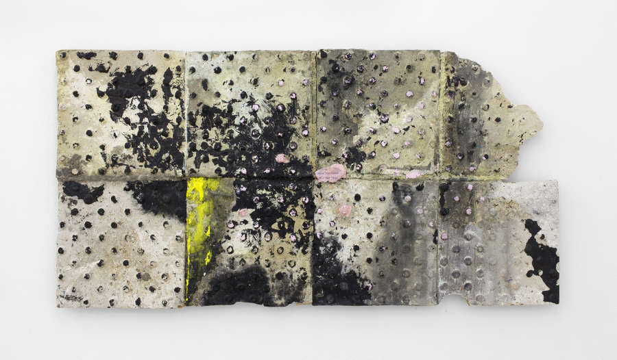 Image of a paper pulp sculpture made by Brandon Ndife that hangs on a white wall. The sculpture is a cast of a subway platform tile with a relief of circular dots. It had a gestural mix of pigment applied to the surface.