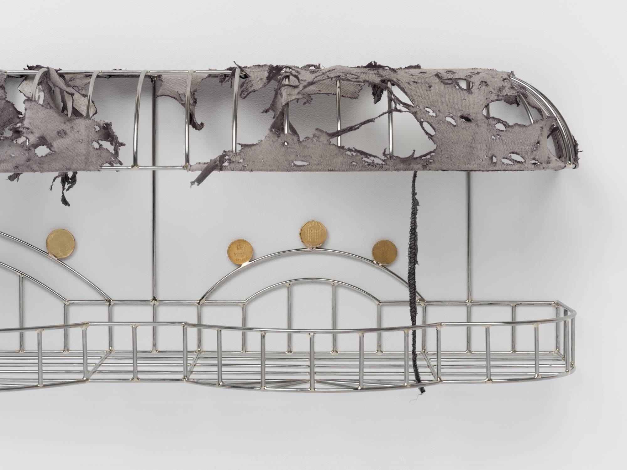 Detail of a cage-like chrome sculpture, wrapped with a tattered grey t-shirt to resemble an awning, and embellished with soldered on gold-colored coins.