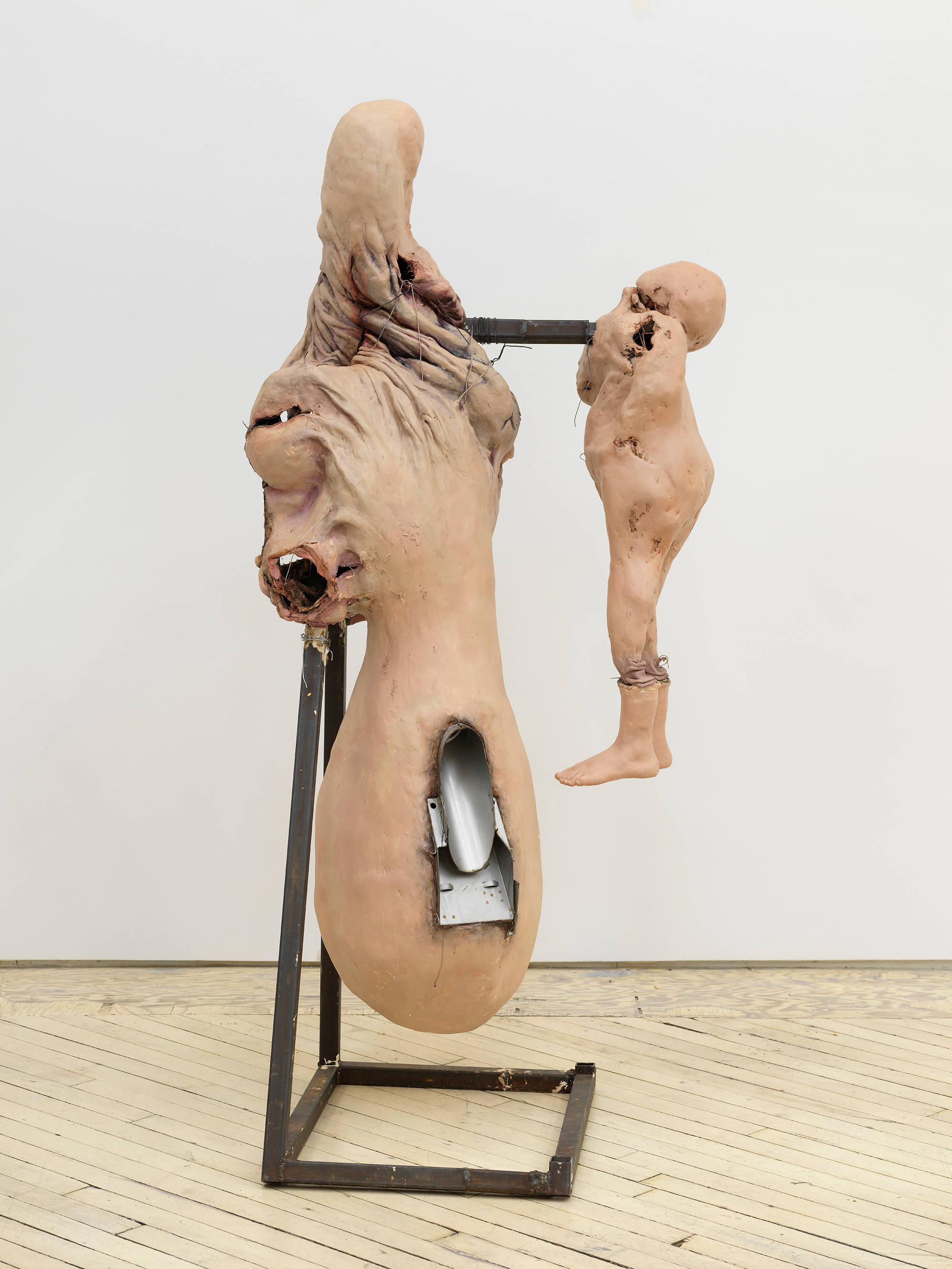 In a gallery space, an abstract sculpture resembling a human form with a steal base.